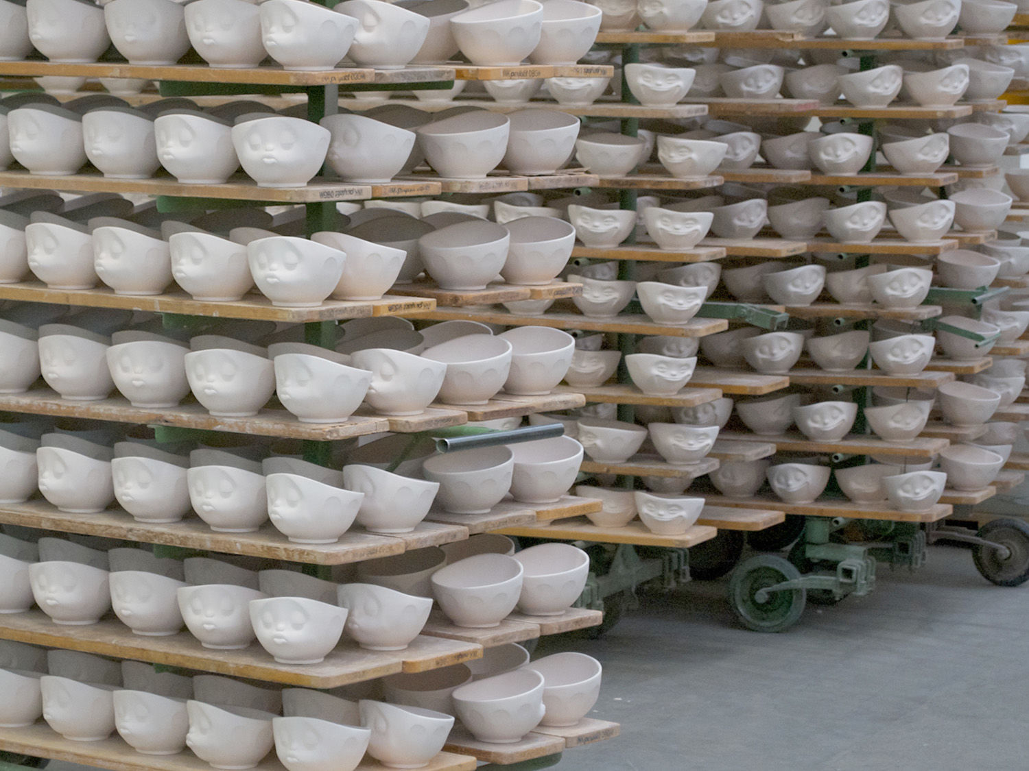  The High Art of Porcelain Manufacturing As the fruits of their labor, BHS tabletop and FIFTYEIGHT PRODUCTS celebrate their first completed production run in 2012. The line is comparatively small at first, featuring four bowls, two coffee cups and two espresso cups. But over the years, the collection would grow to what now amounts to over 40 pieces of porcelain products, while BHS and FIFTYEIGHT continue to raise the bar in terms of product design and manufacturing technology. “At this point it needs to be said that we could never do it without the professionals and artisans on the manufacturing side of things. I have been deeply impressed on numerous occasions by their expertise and the way in which they go to lengths to retain our designs instead of replacing it with production techniques that would be easier to implement,” said Max Zimmermann at FIFTYEIGHT. This kind of time-honored porcelain design expertise, paired with top-of-the-line manufacturing processes – including 70-meters long ovens for firing the porcelain and high-tech burn control – provide BHS tabletop with a unique competitive edge. And in order to maintain it, the company has invested over €50 million in state-of-the-art manufacturing equipment over the past few years. Then again, despite all the technology and high-end gadgetry, porcelain manufacturing ultimately stills boils down to one single thing: skilled craftsmanship. Here’s a quick primer on The High Art of Porcelain Manufacturing… So what does it take to produce porcelain? Basically, porcelain comes from a raw mix consisting of 50 percent Kaolin, 25 percent quartz and 25 percent feldspar. This crystalline mixture is either used as a dry powder or a liquid paste as the basis for four different production methods: Hollow casting. This process relies on turning the design into three-dimensional, hollow casts made from gypsum. Liquid porcelain, also called slip, is then poured into these casts, which serve as a “negative” for the three-dimensional products, including all bowls in the TASSEN series. High-pressure casting. The hollow insides of a cast – in this case crafted from polymer rather than gypsum – are poured with porcelain slip at high pressures. Rotating. Porcelain in a moldable clay form is processed in a rotation method, just picture a lump of clay spinning on a turntable similar to a record player. Shapes and patterns can be added during the spinning process, which is how the large TASSEN salad bowls receives its endearing features. Pressing. Instead of using liquid porcelain slip, a dry granulate powder is processed with an isostatic pressing method. The granulate is inserted into a mould and pressed at pressures upward of 200 bars. The ultimate result of these initial production steps is the so-called body crafted from dry porcelain, which is then headed into the oven for firing. The first round of firing, also called bisque-firing, hardens the raw porcelain at temperatures around 950º C, followed by applying the glaze. During the second round of firing, called glost firing, the glaze hardens as the porcelain becomes solid and dishwasher-safe at 1,420º C. These high temperatures melt together all the separate kaolin, quartz and feldspar grains into a tightly bonded material, safe to be used with foods. This final firing concludes the manufacturing of high-grade porcelain, and the products enter into the polishing and quality approval stages. 